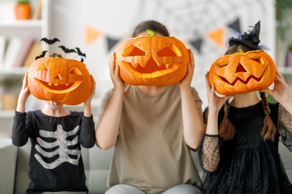 A mother and two children holding up carved pumpkins to their faces.