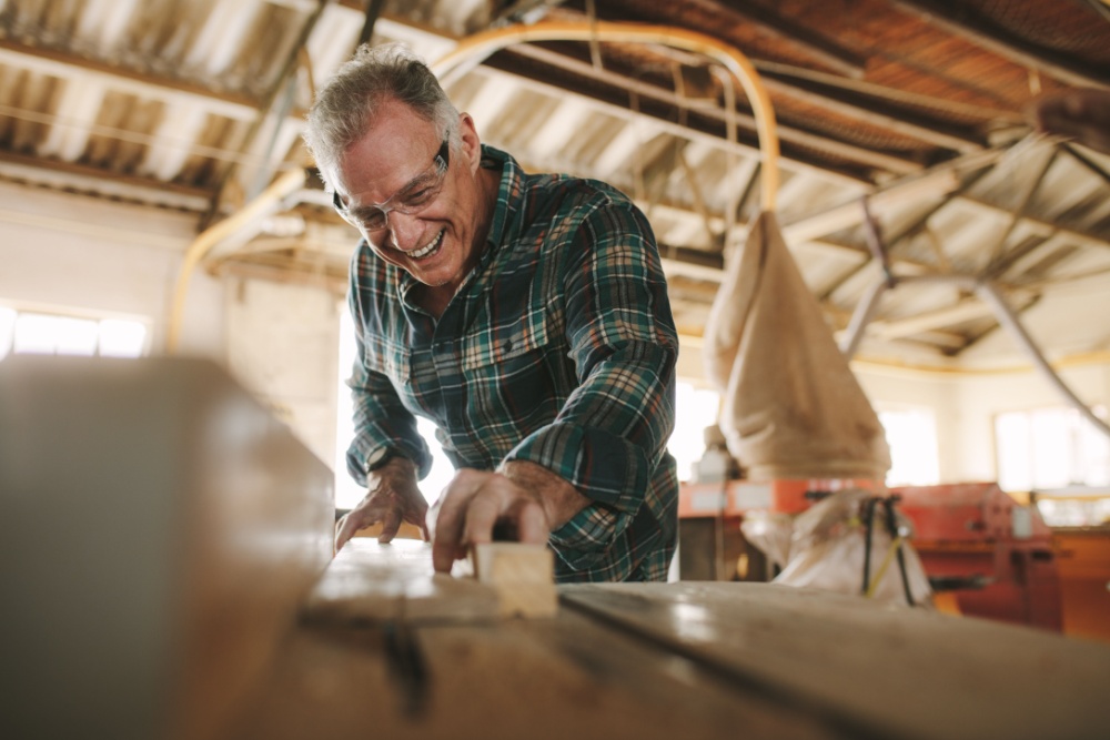 A senior man cutting wooden planks in a workshop.