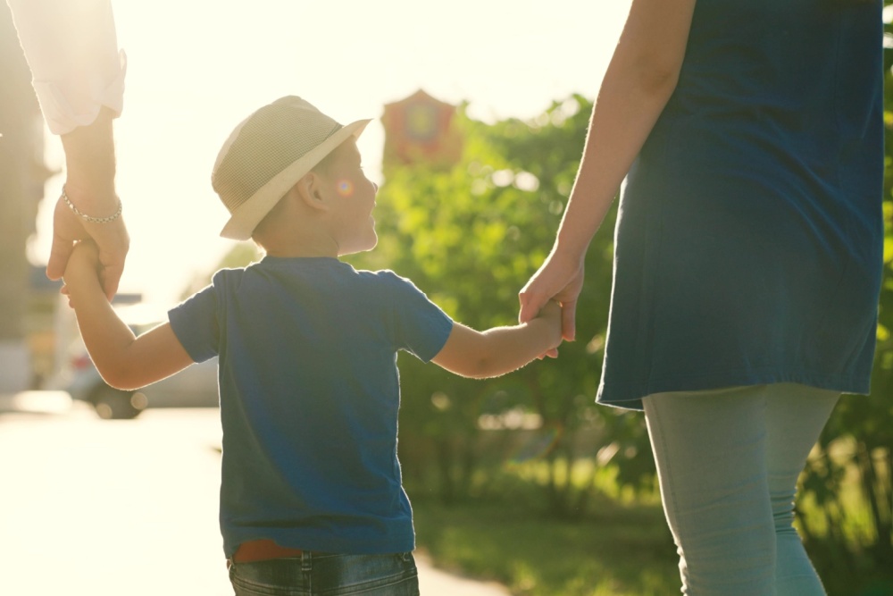 A family with a young child holding hands outdoors.